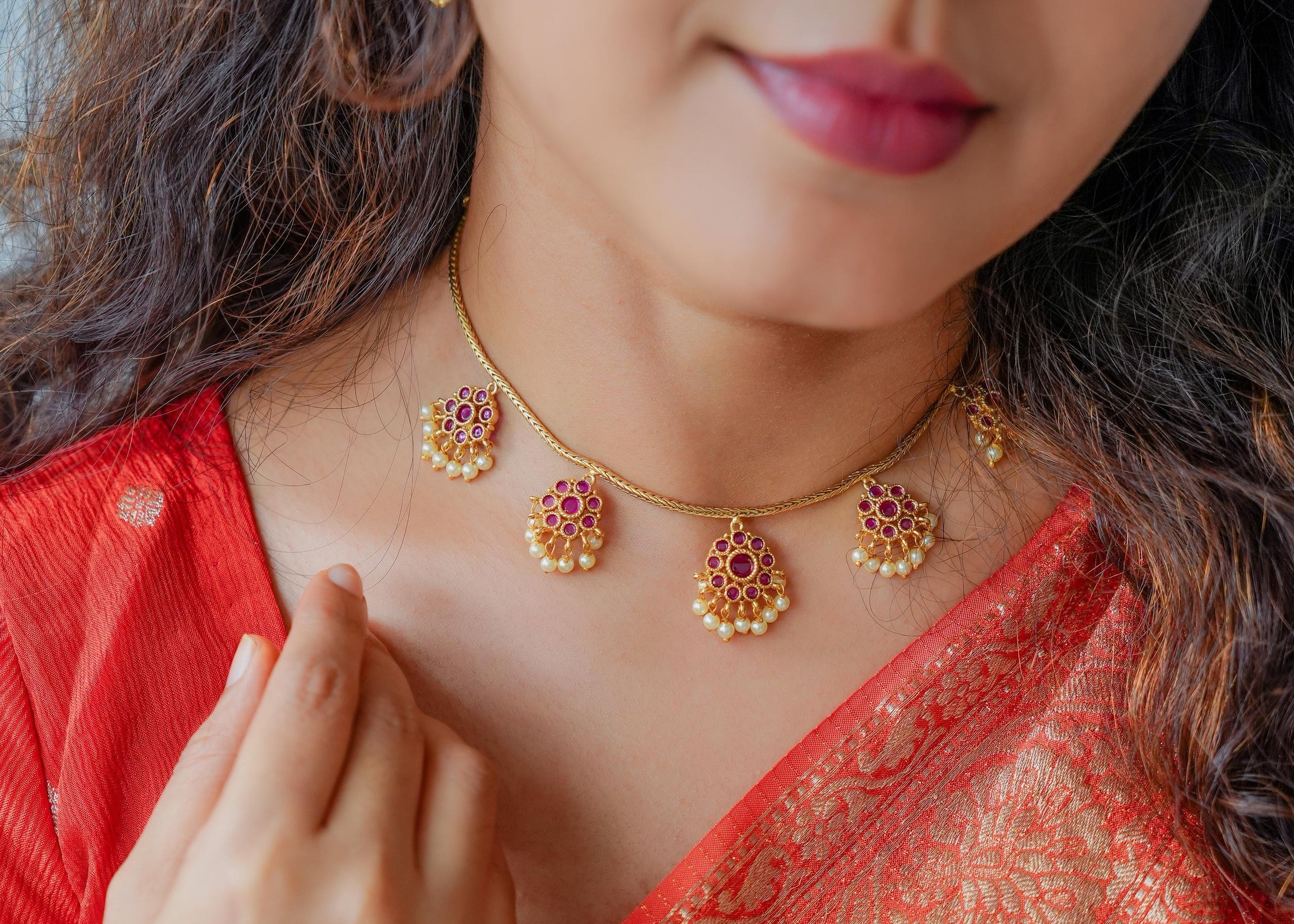 Woman wearing a red saree with gold patterns, gold jewelry, and green bangles.